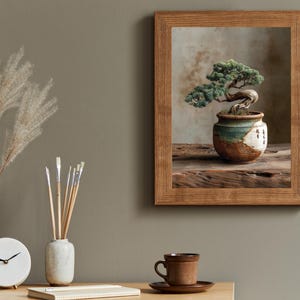 May include: A framed print of a bonsai tree in a ceramic pot with green and white accents. The frame is made of wood. A clock, brushes, and a cup and saucer are on a wooden table.