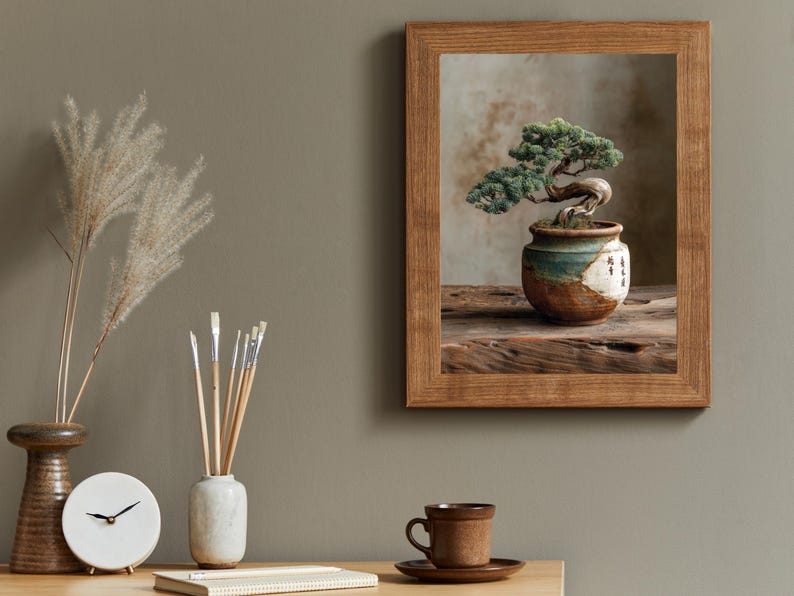 May include: A framed print of a bonsai tree in a ceramic pot with green and white accents. The frame is made of wood. A clock, brushes, and a cup and saucer are on a wooden table.