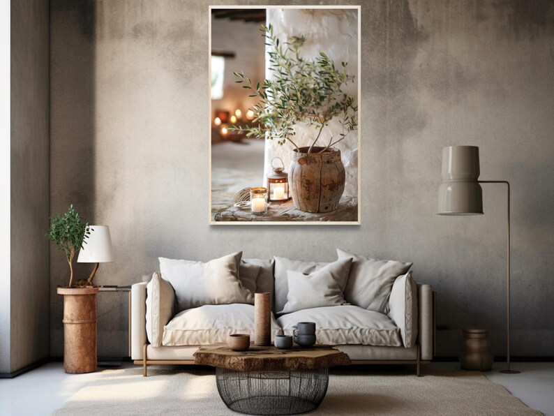 May include: A rustic wooden vase with a green olive branch inside, sitting on a table with two lit candles and a lantern. The vase is in front of a white wall with a window in the background.