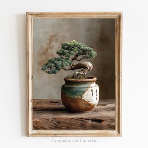May include: Framed print of a bonsai tree in a ceramic pot. The tree has green foliage and a twisted trunk. The pot is a mix of brown, green, and white with Japanese characters. The print is set on a wooden surface.