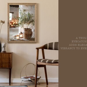 May include: A framed print of a still life featuring a potted olive branch, candles, and a rustic wooden bowl. The print is in a light wood frame and is hanging on a beige wall.