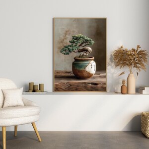 May include: A framed print featuring a bonsai tree in a decorative pot. The bonsai has green leaves and a curved trunk. The pot is brown, white, and teal. The print is displayed on a wooden surface.