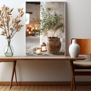 May include: A framed print of a rustic still life featuring a potted olive branch, two lit candles, and a lantern on a wooden surface.
