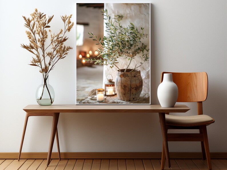 May include: A framed print of a rustic still life featuring a potted olive branch, two lit candles, and a lantern on a wooden surface.