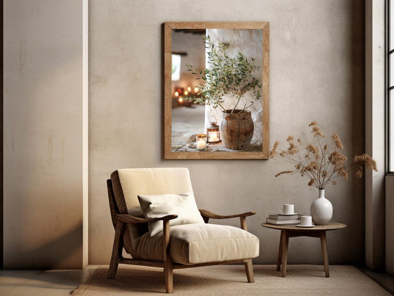 May include: A framed photograph of a potted olive branch with candles in a rustic setting. The photograph is hanging on a wall in a room with a beige armchair and a side table with a vase of dried flowers.