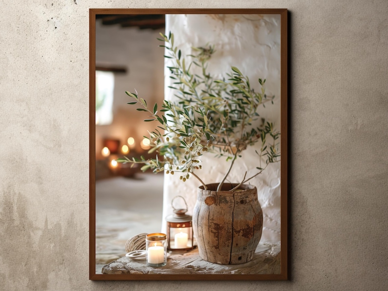 May include: A rustic wooden pot with a small olive tree inside, sitting on a wooden surface with two candles and a lantern. The background is a white wall with a window.