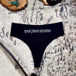 May include: Black underwear with the text "speak friend and enter" printed in white on the front. The underwear is lying on a map of Middle-earth.