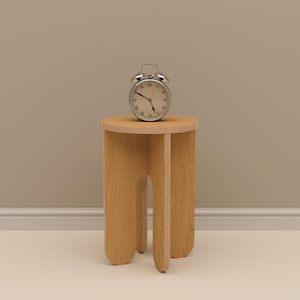 May include: A silver alarm clock with a white face and black numerals sits atop a small, light-colored wooden stool. The stool has a round top and three curved legs. The clock shows the time as approximately 10:10.