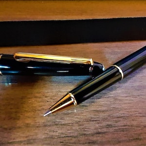 Könnte beinhalten: Ein schwarzer und goldener Stift mit einer einziehbaren Spitze und einem passenden schwarzen Stiftetui.