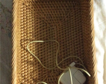 Puede incluir: Una cesta de mimbre tejida con un adaptador eléctrico blanco y un cable en su interior.