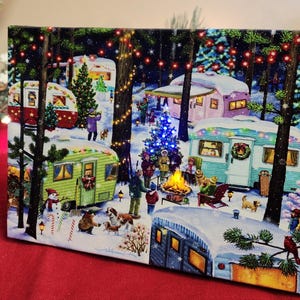 May include: A rectangular Christmas-themed canvas print depicting a winter scene with colorful vintage campers, a bonfire, and people. The print is surrounded by pine branches and fairy lights, creating a festive holiday atmosphere.