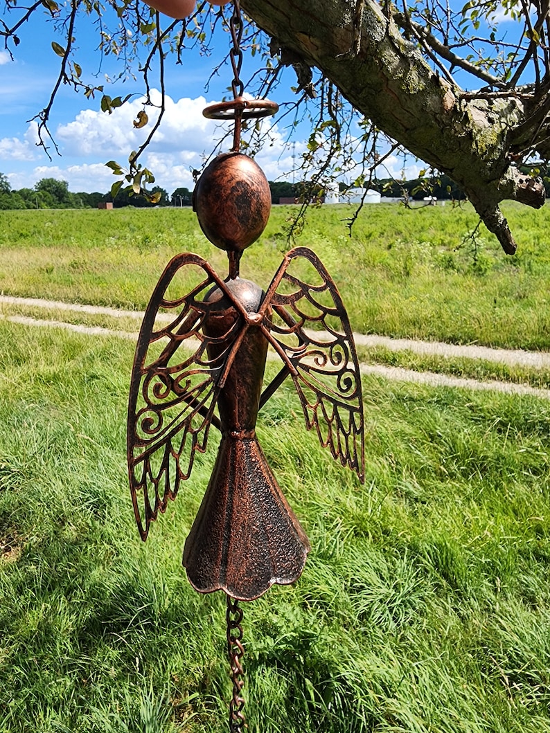 Pu&ograve; includere: Un carillon a vento in metallo color rame a forma di angelo con dettagli intricati sulle ali. L'angelo &egrave; appeso a una catena e ha un'aureola sopra la testa.