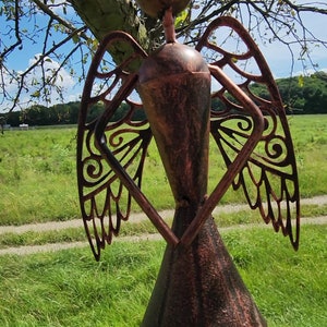 Pu&ograve; includere: Una scultura di angelo in metallo con ali intricate e una finitura in rame anticato. L'angelo &egrave; in piedi in un campo erboso.