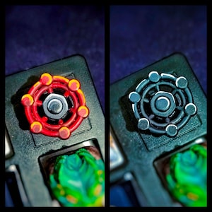 Peut inclure: Deux touches de clavier personnalisées, l'une rouge et jaune, l'autre grise et blanche, sont posées sur un clavier noir. Les touches ont un design circulaire avec un écrou central et des détails. Le fond est sombre.