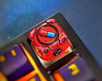 May include: A red and black keyboard keycap with a blue and red pill design. The keycap is a custom design and is made to fit a mechanical keyboard.