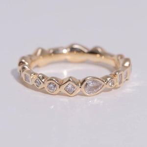 May include: A gold ring with a repeating pattern of diamonds and gemstones in various shapes, including round, square, and pear-shaped. The ring is set against a white background, highlighting its intricate design and sparkle.