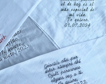 May include: Two white handkerchiefs with embroidered messages in black thread. The first handkerchief says "Papa, de todos nuestros paseos el de hoy es el más especial de mi vida. Te quiero. 01.07.2024". The second handkerchief says "Gracias abu por estar siempre ahí. Ojalá parecerme alguna vez a ti. Te quiere, tu nieto, 2023."