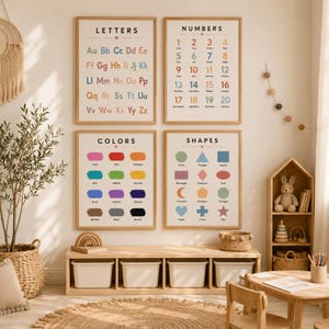 May include: Four educational wall posters in wooden frames featuring Letters, Numbers, Colors, and Shapes with colorful text and illustrations. The posters are arranged in a grid on a light wall above a wooden storage bench with four white bins.