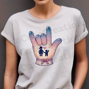 May include: A grey t-shirt with a graphic of a hand making the American Sign Language sign for "I love you". The hand is stylized with a gradient of blue and pink colors. Inside the hand is a small illustration of a woman and a child holding hands with a pink heart above them.