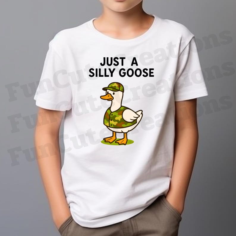 May include: White t-shirt featuring the text "JUST A SILLY GOOSE" and a cartoon duck in a camouflage hat and vest. The duck has a yellow beak and feet. The design is centered on the shirt.