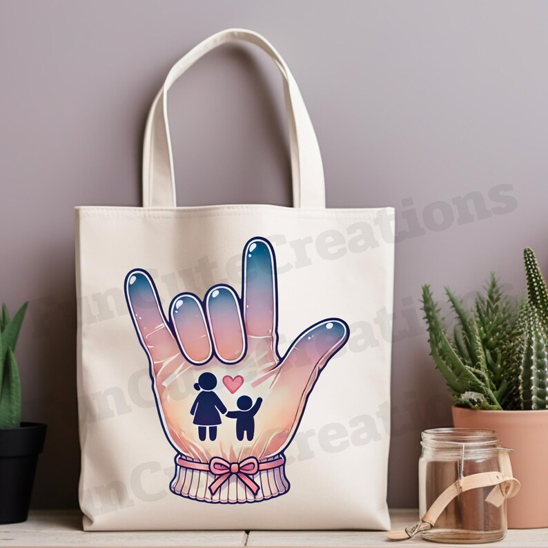 May include: A white canvas tote bag with a pink, blue, and purple hand sign representing the American Sign Language symbol for "I love you". The hand sign has a small illustration of a family with a heart inside.