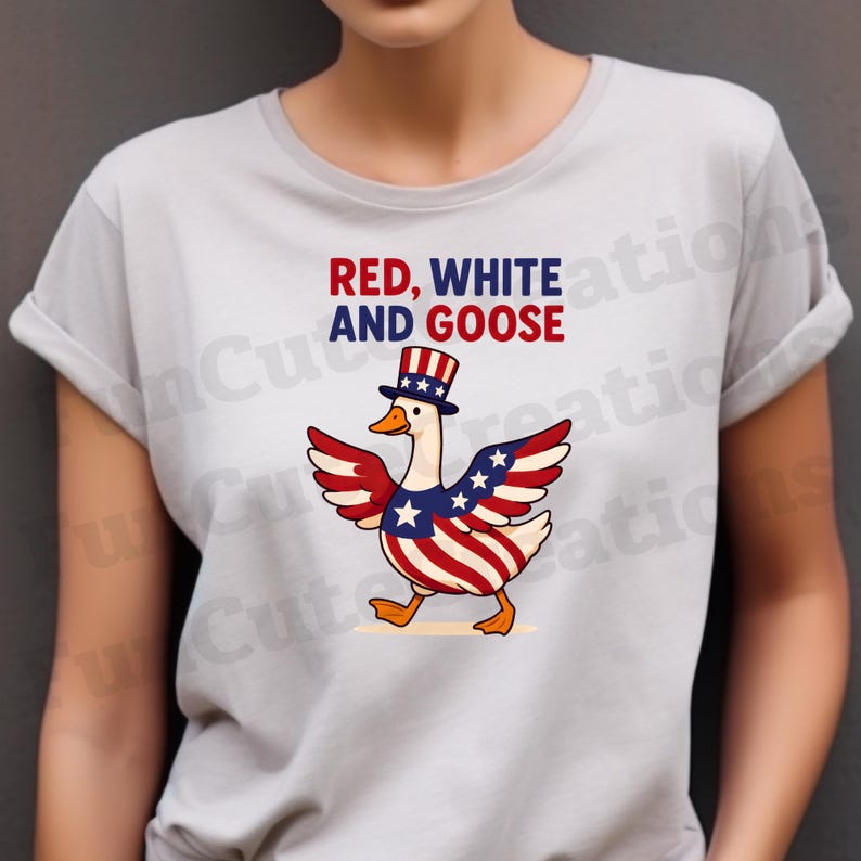 K&ouml;nnte beinhalten: Hellgraues T-Shirt mit einem Cartoon-Gans-Design in Rot, Wei&szlig; und Blau. Die Gans tr&auml;gt einen Zylinder und hat Fl&uuml;gel und K&ouml;rperstreifen in den Farben der amerikanischen Flagge. Der Text "RED, WHITE AND GOOSE" steht &uuml;ber der Gans.