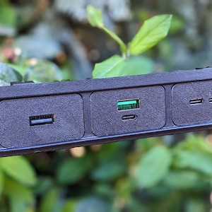 Könnte beinhalten: Nahaufnahme einer schwarzen Kunststoffplatte mit vier Anschlüssen. Die Platte hat einen Knopf mit einem Symbol für die Heckscheibenheizung, einen USB-Anschluss, einen USB-C-Anschluss und zwei Standard-USB-Anschlüsse.