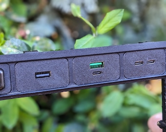 May include: Close-up of a black plastic panel with four ports. The panel has a button with a rear window defroster symbol, a USB port, a USB-C port, and two standard USB ports.