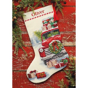 Puede incluir: Un calcetín navideño de color crema con un diseño de punto de cruz de un camión rojo antiguo que transporta regalos envueltos. El camión tiene una corona en la parrilla delantera y el texto SANTA CLAUS en la matrícula. El nombre Oliver está bordado.