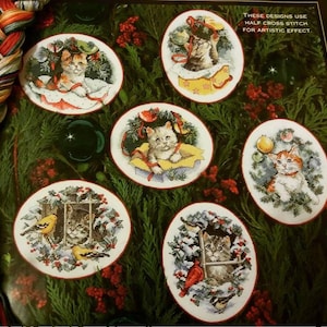 Puede incluir: Una colección de diseños de punto de cruz ovalados con gatos en entornos festivos navideños. Cada diseño muestra un gato, rodeado de decoraciones navideñas como coronas, adornos y cajas de regalo. El texto dice: "Estos diseños utilizan medio punto de cruz para un efecto artístico."