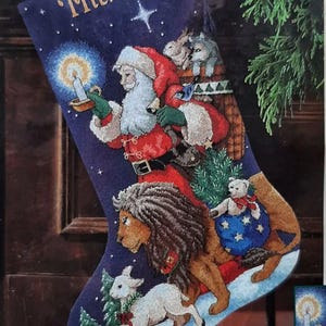 May include: A navy blue Christmas stocking with the name "Michael" embroidered at the top. Santa Claus, a lion, a lamb, and other animals are depicted on the stocking. Santa holds a candle, and the scene is set against a snowy landscape.