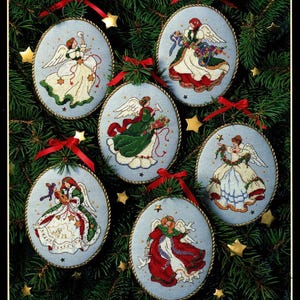 Puede incluir: Seis adornos navideños bordados con ángeles en varios vestidos y poses. Cada adorno ovalado tiene un fondo azul claro, ribete dorado y una cinta roja para colgar. Los ángeles están representados con alas.
