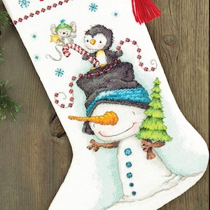 May include: White Christmas stocking with a snowman, penguin, and mouse design. The stocking has the name "SOPHIA" embroidered in red. The snowman has a carrot nose and holds a small Christmas tree. A red tassel hangs from the top.