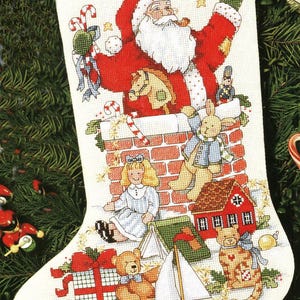 May include: Embroidered Christmas stocking featuring Santa Claus, toys, and the name "MICHAEL". The design includes a chimney, a doll, a rabbit, a house, and various wrapped gifts. The color palette includes red, white, green, and brown.