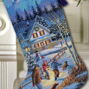 May include: Embroidered Christmas stocking with a winter scene. The stocking is blue with a snowy landscape featuring a house, people, and dogs. The name "Gabrielle" is embroidered at the top. A purple tassel hangs from the top.