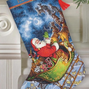 May include: Christmas stocking with a festive design featuring Santa Claus in his sleigh, pulled by reindeer, against a blue night sky. The name "ISABELLA" is embroidered at the top. A red tassel hangs from the top.