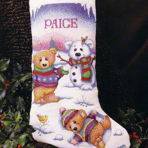 May include: A cross stitch pattern for a Christmas stocking featuring a winter scene with a snowman, a polar bear, and two teddy bears. The stocking is personalized with the name "Paige".