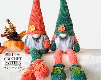Op de afbeelding: Twee pluche kabouters met lange, puntige hoeden, één rood en één groen, elk versierd met een pompoenapplicatie. Ze hebben grijze baarden, ronde neuzen en zitten met bungelende benen. De benen en voeten zijn in tinten groen en oranje. De tekst "PDF CROCHET PATTERN" is zichtbaar.