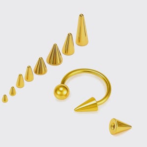 Può includere: Una collezione di gioielli per il corpo color oro, tra cui un bilanciere a forma di ferro di cavallo e diversi borchie a forma di cono di varie dimensioni. I gioielli sono esposti su uno sfondo bianco, mettendo in risalto la finitura metallica lucida.