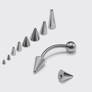 May include: A collection of silver-colored body jewelry, including a curved barbell with a ball end and a conical end, along with several cone-shaped piercing studs of varying sizes. The jewelry is displayed against a white background.