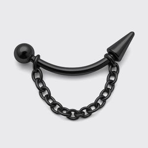 Peut inclure: Boucle d'oreille industrielle noire avec un design de barre incurvée. Une extrémité présente une petite boule, l'autre une pointe conique. Une chaîne pend de la barre, créant un look unique et audacieux. Le bijou est posé sur un fond neutre.