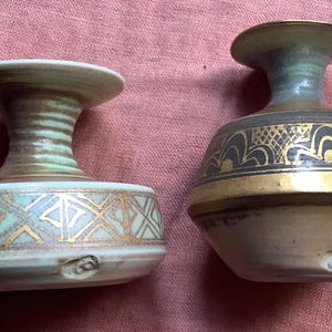 May include: Two ceramic vases with gold accents. The vase on the left has a geometric pattern and the vase on the right has a floral pattern.