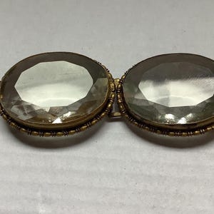 Pode incluir: Broche antigo com duas grandes pedras preciosas ovais e facetadas. As pedras est&atilde;o engastadas numa moldura de metal dourado com detalhes intrincados. Um acess&oacute;rio vintage, provavelmente da era vitoriana ou eduardiana.