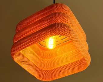 May include: A bright orange pendant light fitting with a square, tiered, and textured honeycomb-like surface. The lamp hangs from a thin black cord and features a single glowing light bulb visible within the centre of the structured shade.