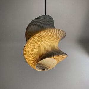 Könnte beinhalten: Eine moderne, abstrakte Pendelleuchte mit einer strukturierten, gewebten Optik. Das Licht hat eine wirbelnde, organische Form mit einem Farbverlauf von Grau zu warmem Gelb. Sie hängt an einem schwarzen Kabel.