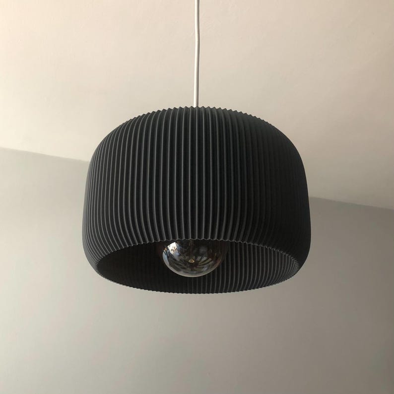 May include: A black pleated pendant light fixture with a round, ribbed shade. The light is hanging from a white cord.