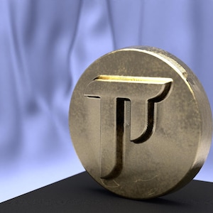 May include: A gold-colored, circular coin or medallion with a stylized letter "T" design. The coin is set on a black surface against a soft, blue background. The coin has a textured surface and a slightly worn appearance.