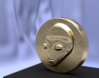 May include: A gold-coloured coin with a detailed relief of an alien face. The coin is round with a raised edge and sits on a black surface against a soft blue background. The alien's face has large eyes and a smooth, rounded head.