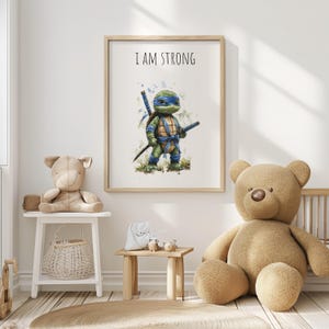 May include: A framed print with a cartoon turtle character in blue and green, holding swords. The text "I AM STRONG" is above the character. The artwork is in a light wood frame, suitable for a child's bedroom.