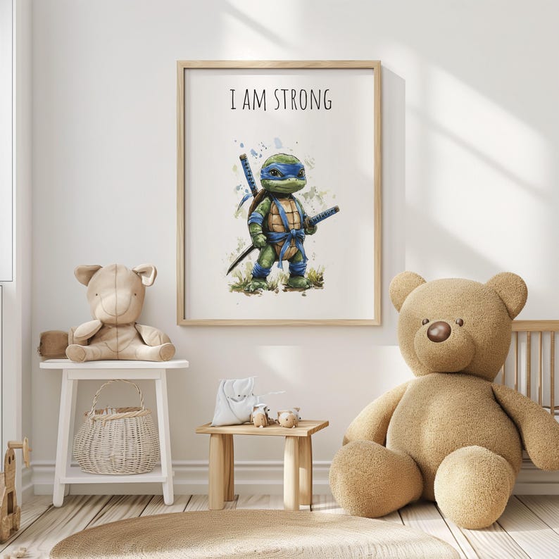 May include: A framed print with a cartoon turtle character in blue and green, holding swords. The text "I AM STRONG" is above the character. The artwork is in a light wood frame, suitable for a child's bedroom.